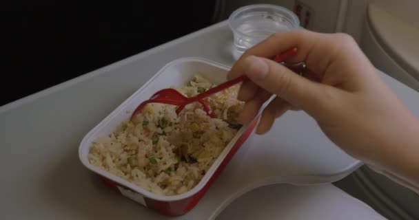 No avião na mesa é utensílios de mesa descartáveis com um prato de arroz e frango e uma mulher come comida com um garfo — Vídeo de Stock