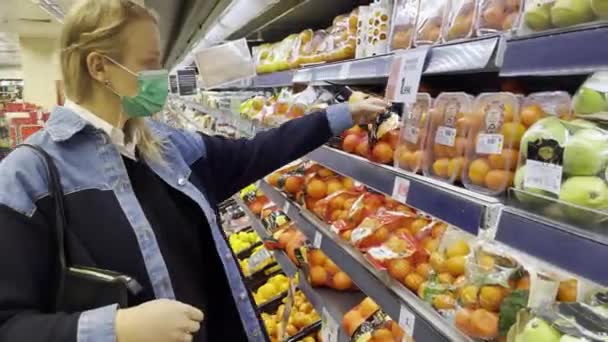 Молодая женщина покупает фрукты в магазине во время пандемии — стоковое видео