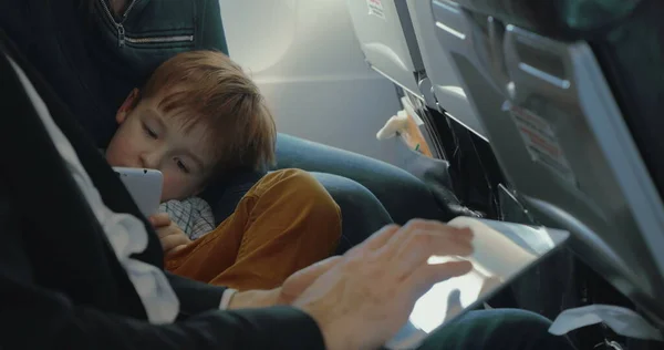 Мальчик с помощью смартфона и отца с планшетом в самолете — стоковое фото