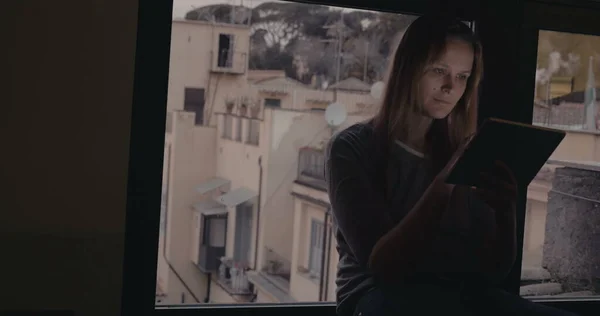 Woman using tablet PC sitting on windowsill — Stock Photo, Image