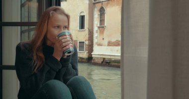 Wistful woman having coffee at home in Venice clipart