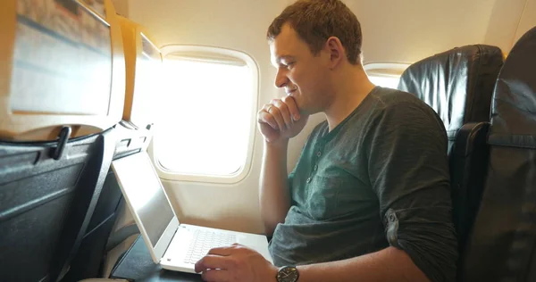 Young man chatting on laptop in the plane — Stock Photo, Image