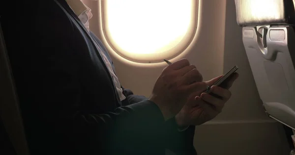 Hombre usando pluma para escribir en el teléfono inteligente en avión —  Fotos de Stock