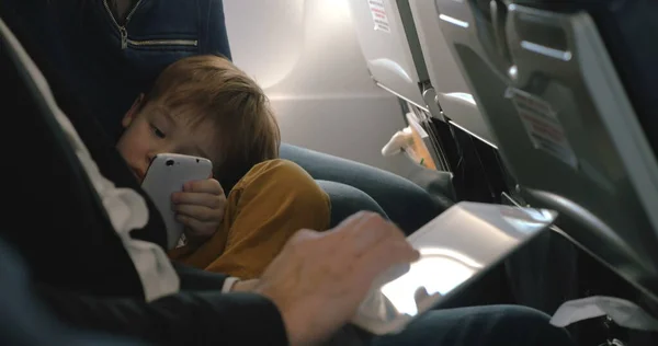 Child with cell and and and man using pad in plane — стоковое фото