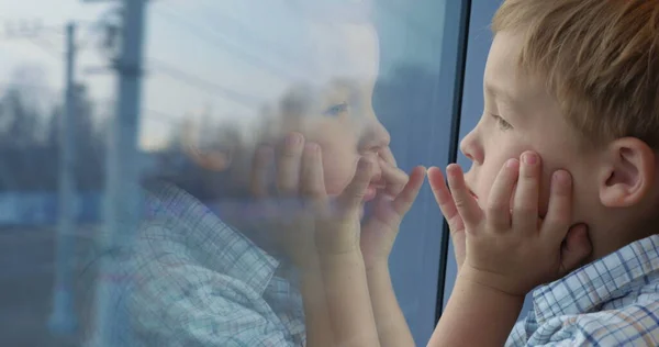 Chico mirando por la ventana del tren con las manos en la cara — Foto de Stock