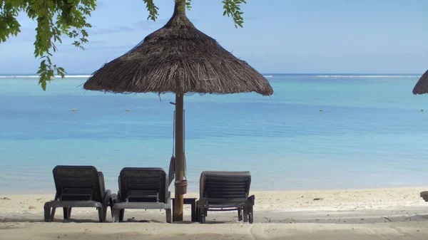 Uitzicht op lege chaise-longue nabij inheemse parasol tegen blauw water, Mauritius Eiland — Stockfoto