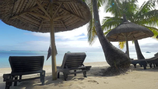 Vista de la chaise-longue vacía cerca de sombrilla nativa y palmeras contra el agua azul, Isla Mauricio — Foto de Stock