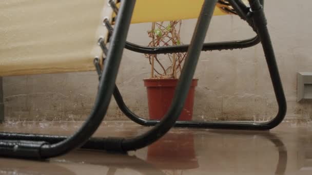 Una silla amarilla y una flor se están mojando en el balcón bajo la lluvia — Vídeos de Stock