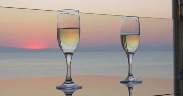 Nő és férfi kezét csengő poharak Champagne-i naplemente tengeri háttér, zár megjelöl kilátás — Stock Fotó