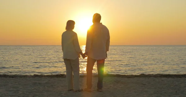 Amar pareja de ancianos disfrutando de la puesta de sol sobre el mar — Foto de Stock