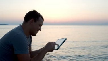 Sahilde tablet bilgisayar kullanan adam