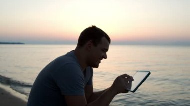 Sahilde tablet bilgisayar kullanan adam