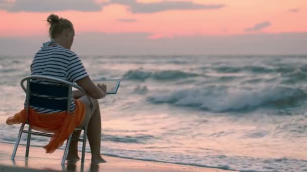 Mujer con almohadilla sentada en silla por mar — Vídeos de Stock