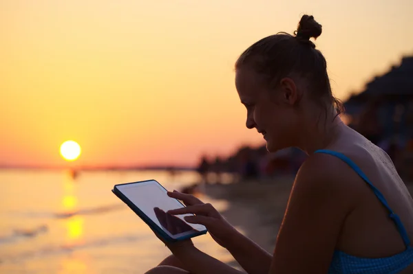 Donna sorridente utilizzando pad sulla spiaggia al tramonto — Foto Stock