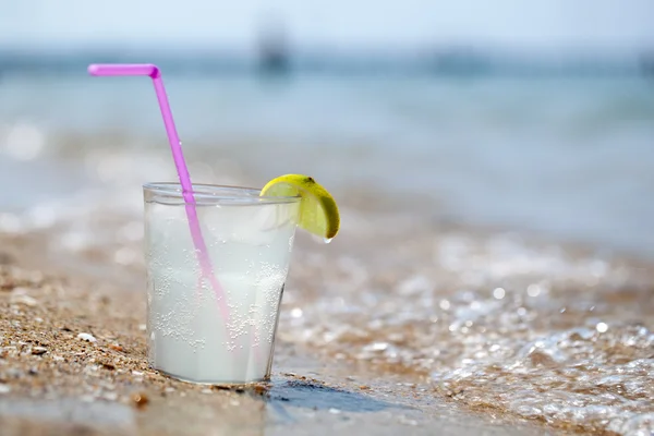 Glass of lemonade or water on beach by sea — Stock Photo, Image