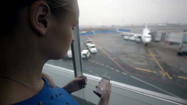 Žena poslechu hudby oknem na letišti — Stock video