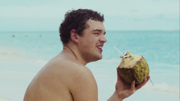 Чоловік на пляжі п'є з кокосу — стокове відео