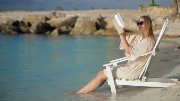 Жінка з майданчиком робить фотографії моря, сидячи на стільці на пляжі — стокове відео