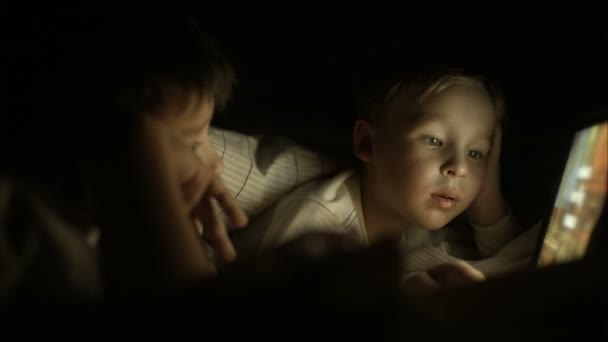 Два мальчика, лежащих в постели по ночам и пользующихся планшетом — стоковое видео