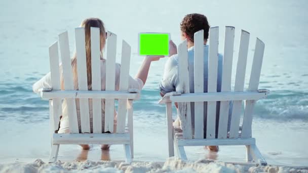 Mulher e homem sentados na praia e olhando para almofada com tela verde — Vídeo de Stock
