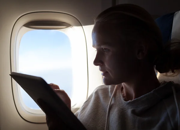 Woman sitting by illuminator in plane with touch pad — Stock Photo, Image