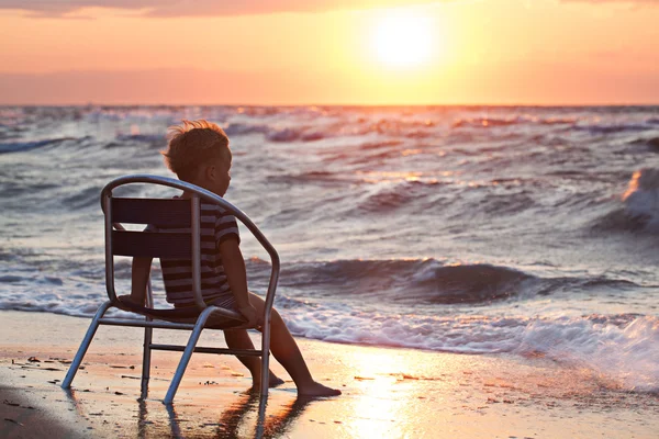 Lilla barnet tittar på solnedgången sitter vid havet — Stockfoto