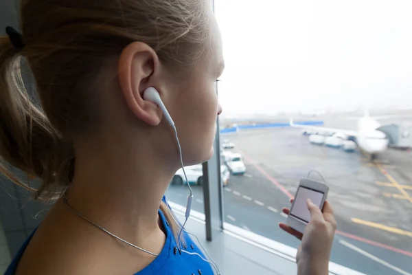 Kvinna som lyssnar på musik vid fönstret på flygplats — Stockfoto