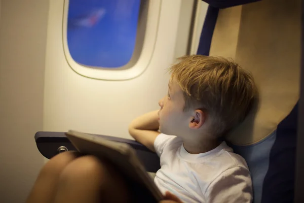 Boy in plane looking out illuminator with pad on lap — Stock Photo, Image