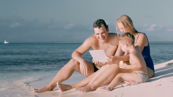 Šťastná rodina ze tří sedí u moře a použití podložky