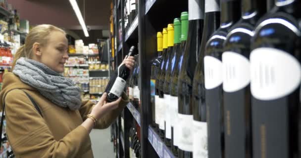 Mujer en la tienda eligiendo botella de vino — Vídeo de stock