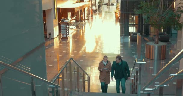 Young couple with pad going upstairs in modern trade centre — Wideo stockowe