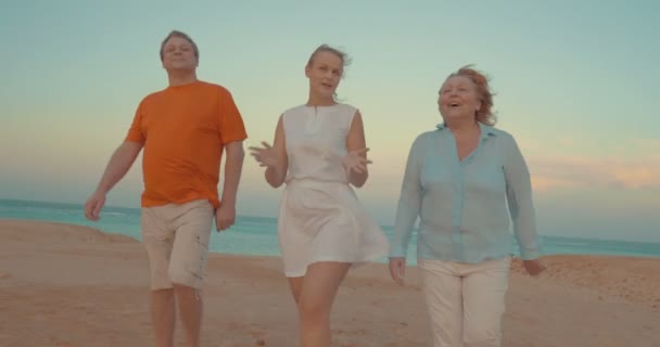 Молодая женщина и родители прогуливаются по пляжу — стоковое видео
