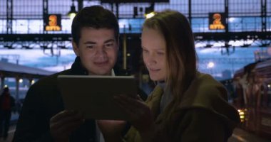 Young people using pad at station in the evening