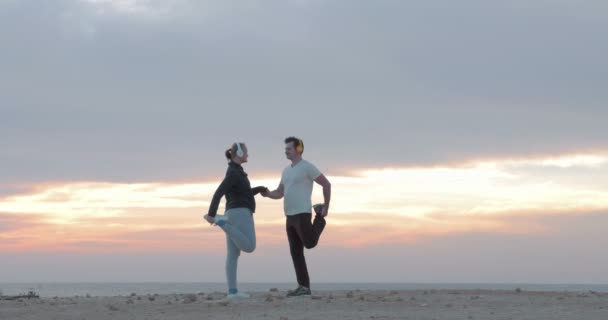 Young people in headphones exercising on the beach — Stockvideo