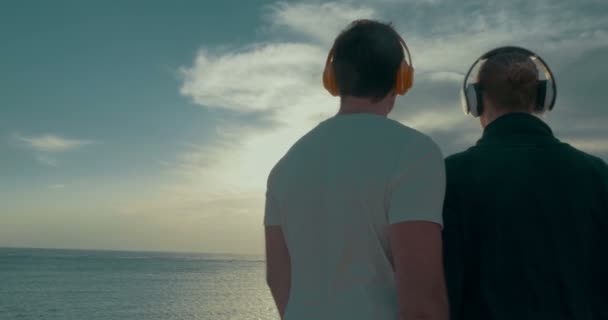 Pareja joven en auriculares disfrutando de la escena del mar y el cielo — Vídeos de Stock