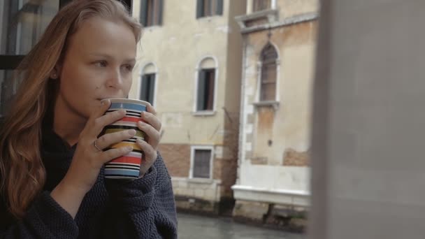Женщина наслаждается горячим чаем и видом на улицу — стоковое видео
