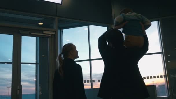 Young family looking out airport window at sunset — Stock video