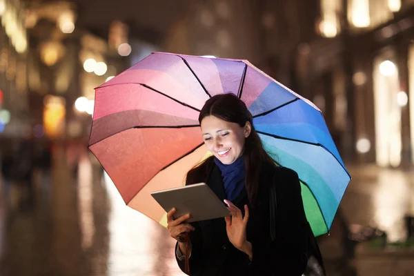 Woman using pad under umbrella in the evening city — Stock Photo, Image