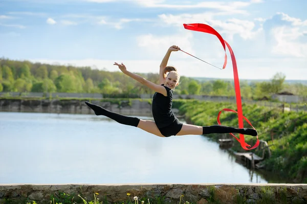 Gymnast girl doing leg-split in a jump with ribbon — Stock Photo, Image