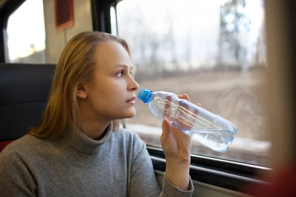 Frau trinkt Wasser und schaut aus Zugfenster — Stockfoto