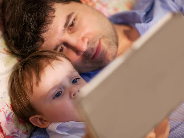 Man and little boy playing with tablet in bed — Stockfoto