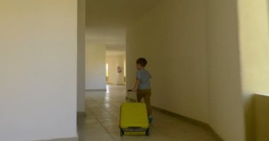 Otel koridoru boyunca uzanan haddeleme çantası ile çocuk