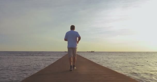 Muž při západu slunce běhat po molu — Stock video