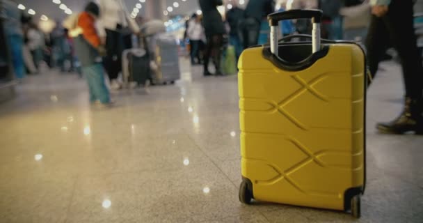 Yellow suitcase on the floor at crowded airport — Stockvideo