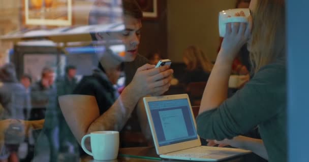 Молодые люди со смартфоном и ноутбуком в кафе — стоковое видео