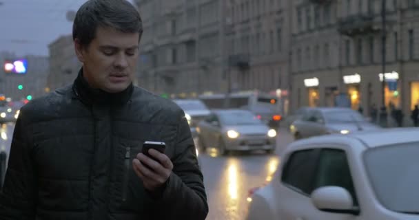 Hombre con celular en la ciudad lluviosa de la noche — Vídeo de stock