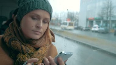 Woman using phone in bus on rainy day