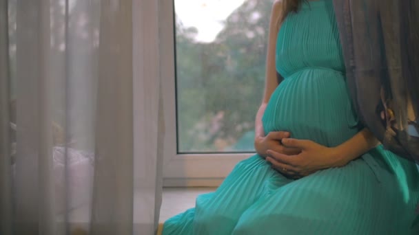 Pregnant woman sitting on windowsill and embracing belly — Stock Video