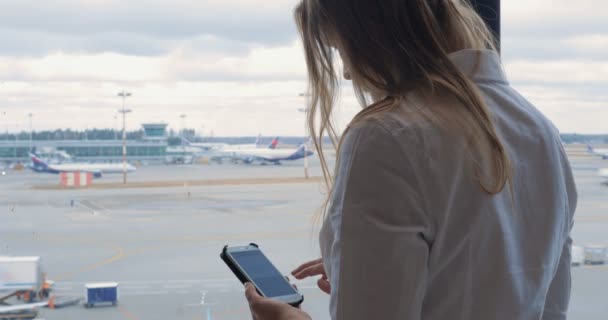 Mujer mensajes de texto en la celda y mirando el área del aeropuerto — Vídeos de Stock