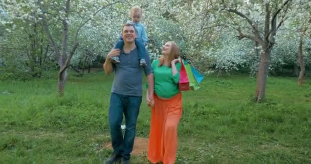 Famille heureuse avec enfant marchant dans un parc fleuri — Video